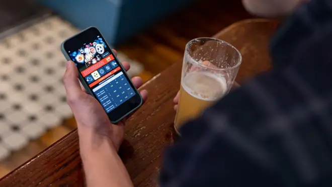 Homem tomando cerveja e fazendo apostas onlinelampions bet aplicativocelular