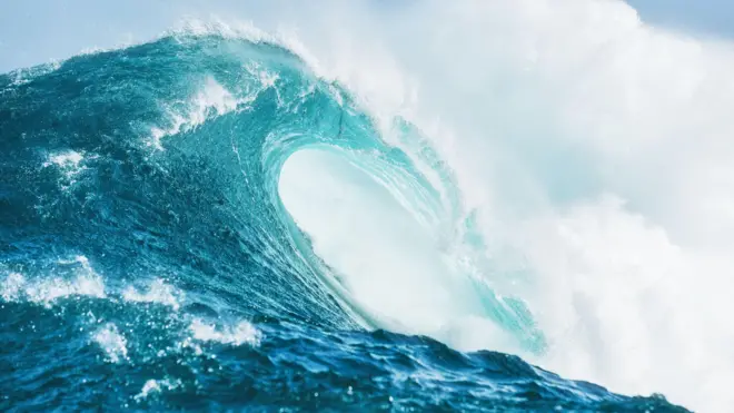 Close up detail of powerful teal blue wave breaking in open ocean on a bright sunny afternoon