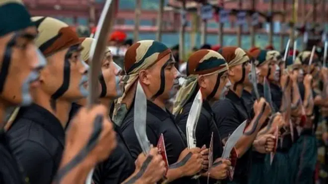 खुकुरी हातमा बोकेका र कालो पोशाक र सैनिक रुमाल टाउकोमा बाँधेका गोरखा सैनिकहरू लामबद्ध अवस्थामा 