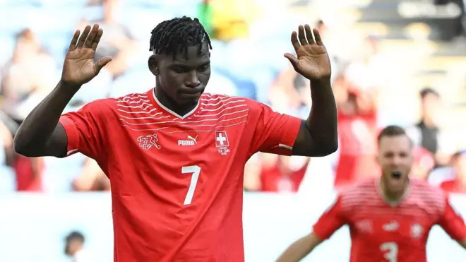Breel Embolo dari Swiss, mengenakan kaus merah bernomor tujuh, mengangkat tangannya setelah mencetak gol melawan Kamerun, negara kelahirannya, di Piala Dunia 2022