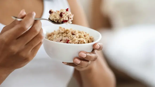 Une femme tenant une cuillère remplie d'avoine et un bol 
