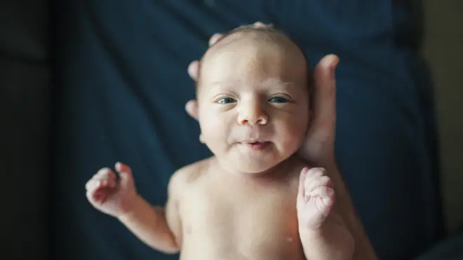 Bebê pequeno temaposta ganha telefonecabeça segurada por mão humana e olha diretamente para a câmera