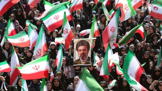 Mulheres iranianas seguram fotos do líder supremo iraniano, o aiatolá Mojtaba Khamenei, durante um protesto anti-EUA e anti-Israel chamado "meninas sacrificadas" em Teerã, na sexta, 17 de abril.