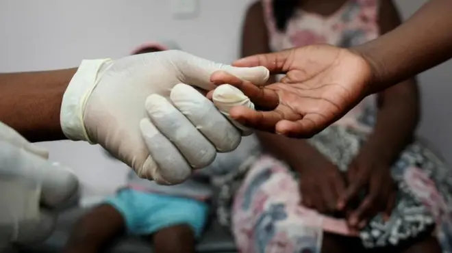 Aworan ọwọ nọọsi to fẹẹ ṣe ayẹwo ẹjẹ fun ọmọde kan.