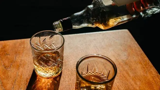 Masa üzerinde iki içki kadehi, birine şişeden içki boşaltılıyor