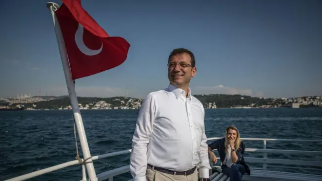 Ekrem İmamoğlu Boğaz'da teknede, yanında Türk bayrağı var. Eşi Dilek İmamoğlu arkada gülüyor