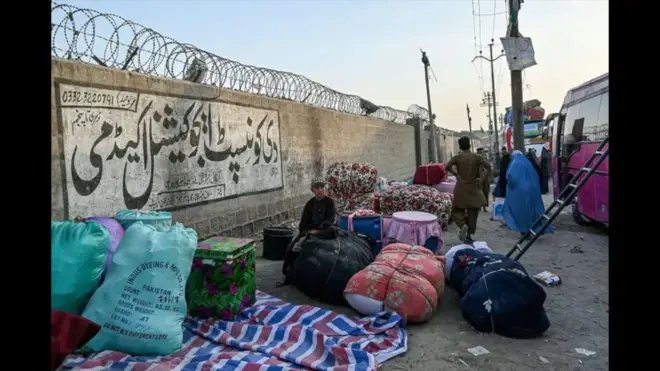 یک خانواده مهاجر افغان وسایل منزلشان را کنار دیوارچیده و منتظر بار زدن به بس مسافربری هستند.