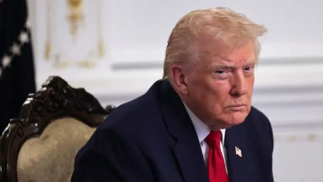 金色の布張りの椅子に前かがみの姿勢で座ったトランプ氏が、険しい表情で、目だけ動かして左を見ている。