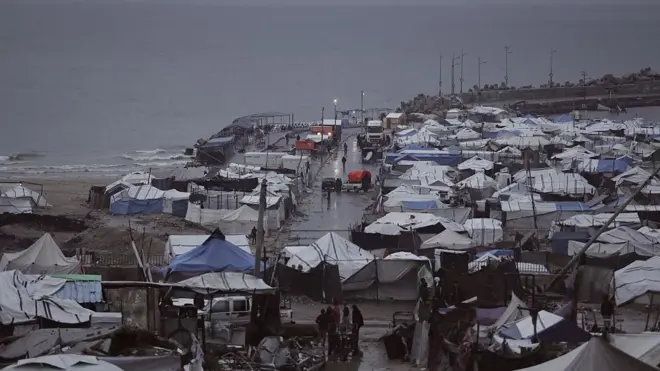 İsrail saldırıları nedeniyle yerlerinden edilen Filistinliler, 15 Aralık 2025'te Gazze şehrinde derme çatma çadırlarda hayatta kalma mücadelesi veriyor. Kapalı havada onlarca derme çatma çadır, ileride deniz görünüyor. 