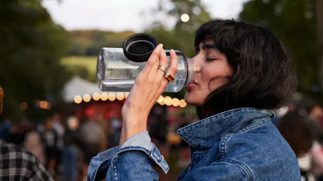 Seorang perempuan minum air dari botol plastik yang bisa digunakan berulang-ulang.
