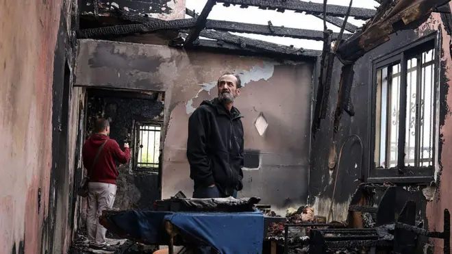 হামলার পর পুড়ে যাওয়া বাড়ির ধ্বংসাবশেষ দেখছেন একজন ফিলিস্তিনি ব্যক্তি 