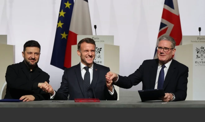 Zelenskiy, Macron ve Starmer oturdukları kürsüde el sıkışıyor ve hallerinden çok memnun görünüyorlar.