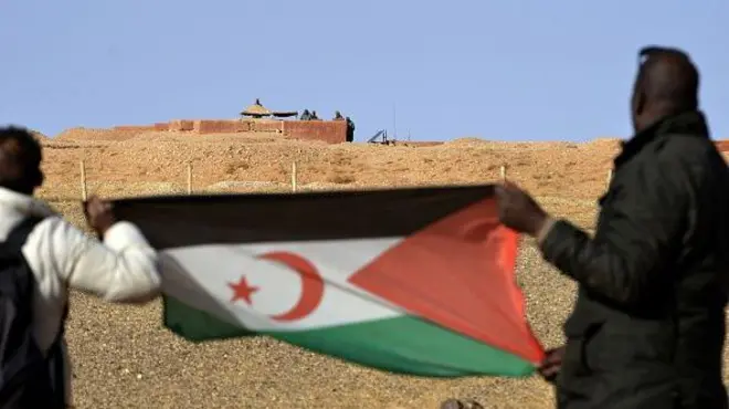 صحراويان يحملان علم الصحراء الغربية أمام الجدار الفاصل بين شطري الإقليم 