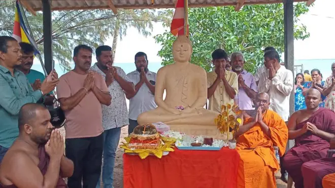 නැවත තැන්පත් කළ බුදු පිළිමය අසල අසුන්ගෙන පිරිත් කියන ස්වාමින් වහන්සේලා සහ සිටගෙන සිටින බැතිමතුන් 