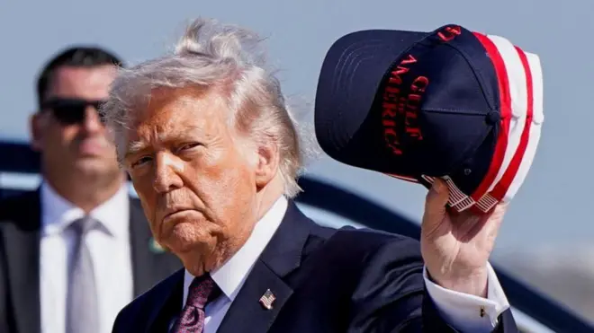 屋外に立つトランプ氏。手に、「アメリカ湾」と書かれたキャップを持っている