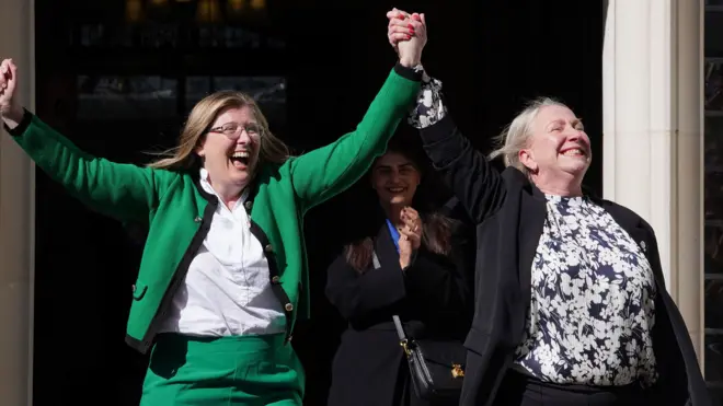 Two women hold hands in the air in celebration in a doorway