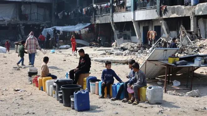 Children sit next to water cans at a school turned shelter in Jabalia, Gaza, on 4 February 2025