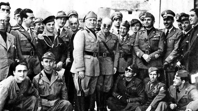 Mussolini posa rodeado de hombres uniformados sonrientes. 