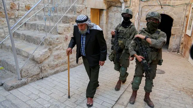 شيخ فلسطيني وخلفه جنديان إسرائليليان بمدينة الخليل بالضفة الغربية المحتلة 