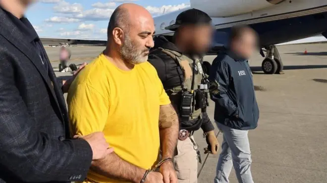 رضا دیندار با تی‌شرت زرد دستبند به دست در حال استرداد به آمریکا