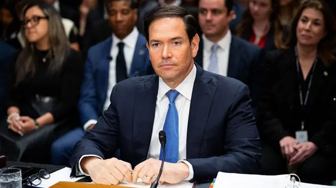 Marco Rubio masada, mikrofon başında oturuyor. 