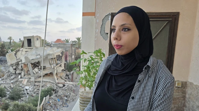 Hanya, who is wearing a black headscarf, looks out at a street filled with destroyed buildings from her balcony