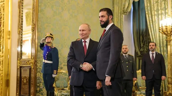 Putin ve Şara, üzerlerinde takım elbiselerle ayakta el sıkışırken arkalarında bir sarayın gösterişli iç dekorasyonu ve ayakta duran görevliler yer alıyor. İki lider de aynı renklerde takım elbise giymiş: Koyu ceket ve pantolon, beyaz gömlek ve kırmızı kravat