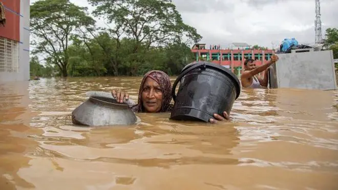 A woman and a man carry relief supplies through floodwaters on August 24, 2024 in Feni, Bangladesh
