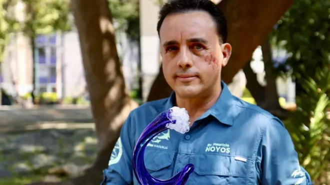 Mauricio mira a la cámara, mientras sostiene un premio en forma de ola. 