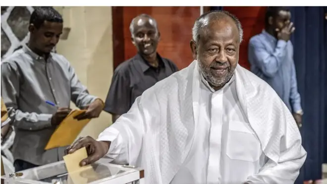 Aarẹ Omar Guelleh nigba to n dibo, o wọ aṣọ funfun, o n rẹrin-in, awọn ọkunrin mẹta kan wa lẹyin rẹ ninu aworan yii.