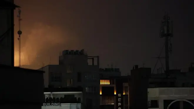 夜の暗い市街地の一角がオレンジ色に光り、煙が上がっている