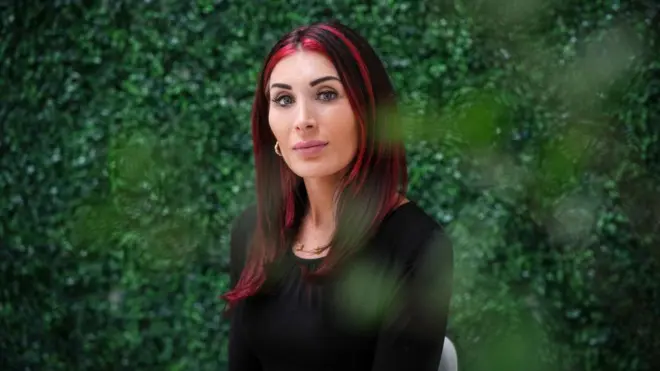 Лора Лумер, жінка з довгим темним волоссям, в якому видно червоні пасма