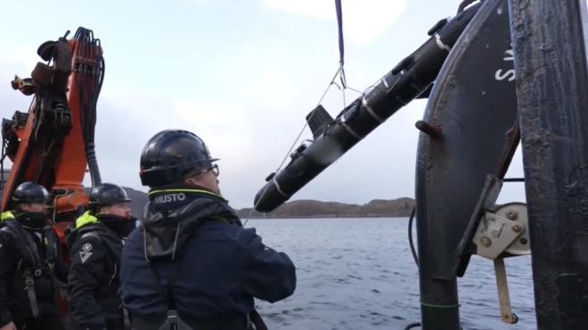 Трое мужчин в касках на борту корабля спускают в море глайдер с помощью лебедки