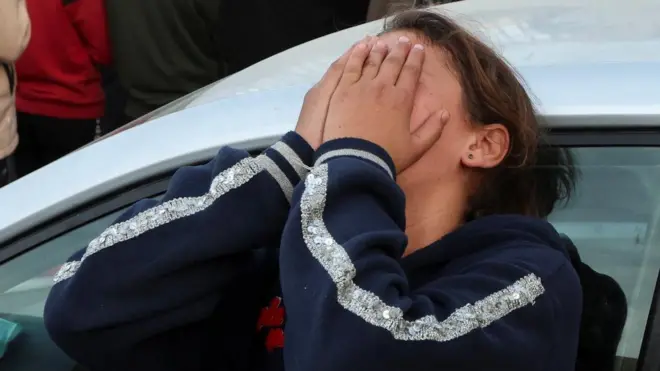 両手で顔を覆い、白い車に寄りかかり嘆く若者