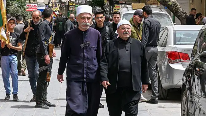 Dürzi ve Hristiyan nüfusunun ağırlıkta olduğu Şam banliyösü Ceramane'deki Syouf Meydanı yakınlarında silahlı kişiler nöbet tutuyor. Önde Dürzi azınlıktan kişiler var, arkalarındaysa en az iki uzun namlulu silah taşıyan kişi var.