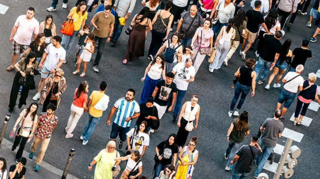 Dziesiątki osób, głównie młodych, przekraczają ruchliwą ulicę w ciepły, słoneczny dzień. 