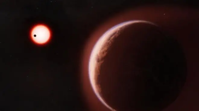 Representación artística del exoplaneta LHS 1140b, un gran planeta rocoso de color marrón rojizo que ocupa el primer plano, bordeado por un tenue resplandor atmosférico blanco azulado. En el fondo oscuro, una pequeña estrella roja brilla intensamente, con un segundo planeta más cercano mostrado como una diminuta silueta negra que cruza frente a él.