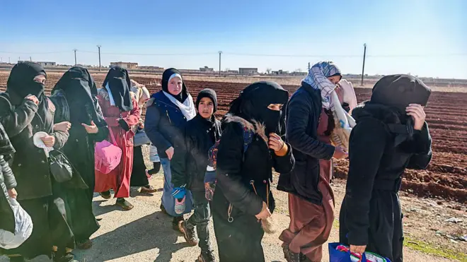 Kırsaldaki bir yolda sekiz kadın ve bir çocuktan oluşan kalabalık hareket halinde, eşyalarıyla birlikte yürüyorlar. 