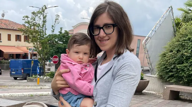 Valentina, a woman with dark hair and glasses, holds a baby in a pink jumper