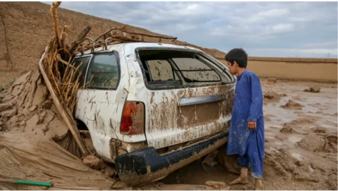 عکسی از سیلاب ویرانگر در افغانستان. پسری به یک موتر گیر مانده در گل ناشی از سیلاب میبیند