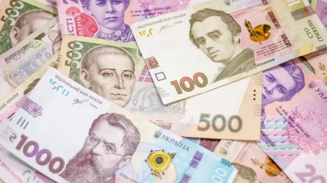 На малюнку внизу ліворуч зображена купюра "1000 гривень", в центрі - купюра "500 грн", праворуч - купюра "100 грн". На задньому плані є інші купюри, зокрема дві купюри по 200 грн 