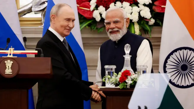 Путин и Моди пожимают друг другу руки на фоне флагов России и Индии.