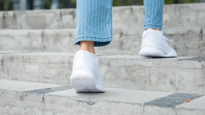 Unos pies con calzado deportivo blanco subiendo escalones en lugar indefinido