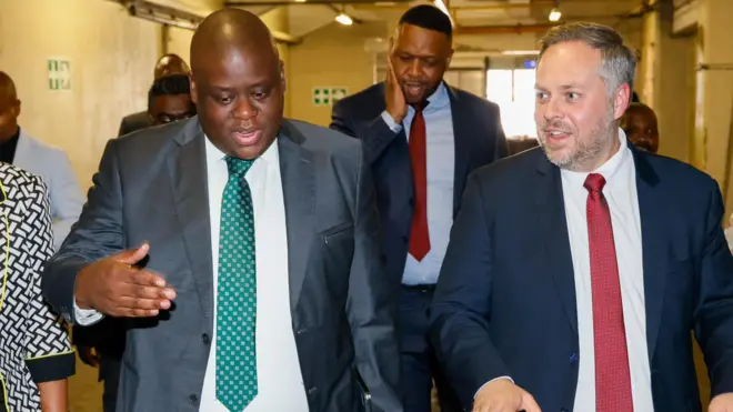 Home Affairs Minister Leon Schreiber wear white tie and di Deputy Nzuza wear green tie wit suit wen dem visit di govment Printing Works