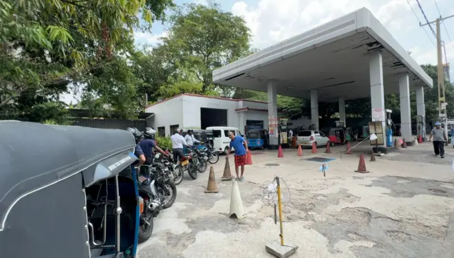 ඉන්ධන පිරවුම්හලක යතුරුපැදිකරුවන් විශාල පිරිසක් සිටින අතර ත්‍රීරෝද රථයක්ද තිබේ.