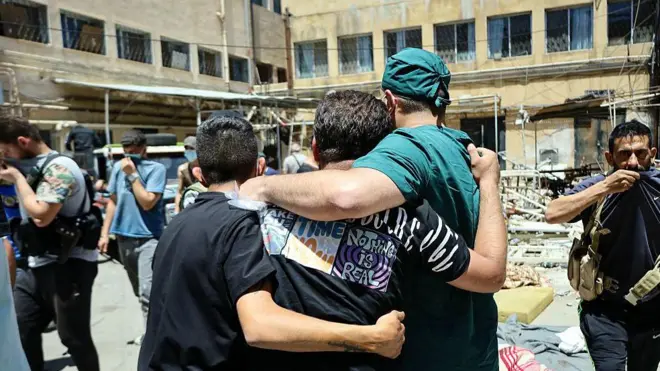 Un trabajador sanitario y otros hombres caminan por el patio de un hospital, junto a los cadáveres de las víctimas de los recientes enfrentamientos en la ciudad meridional siria de Sweida, el 17 de julio de 2025.