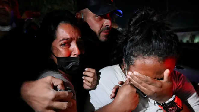 Un grupo de familiares y amistades reaccionan durante un operativo de rescate en La Guaira, Venezuela. Un hombre abraza a una mujer visiblemente conmocionada y otra se cubre la cara con la mano llorando. 27 de junio 2026