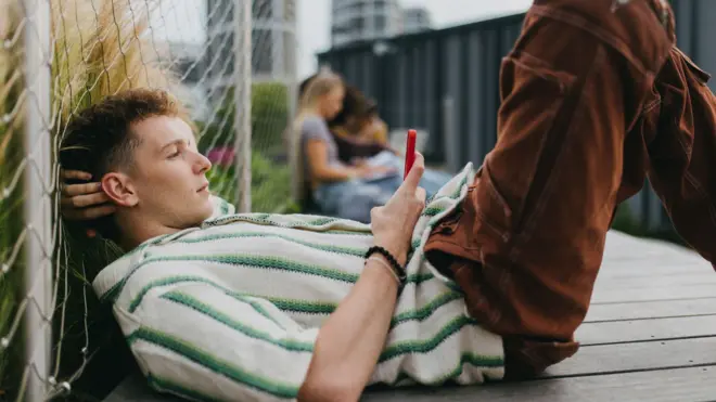 地面に横たわり、スマートフォンを手に持って画面をスクロールしている若い男性の写真