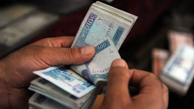 دوه لاسونه ښکاري چې د افغانیو پنځهسوییز بنډل شماري.