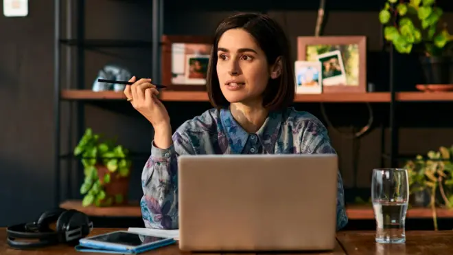 Жінка працює віддалено, тримаючи ручку і задумливо сидячи за столом